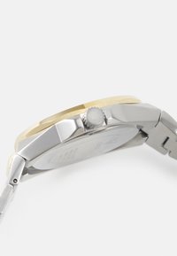 Silberne und goldfarbene Armbanduhr mit einem Armband aus Edelstahl, achteckigem Gehäuse, strukturiertem Lünette und einer Krone auf der rechten Seite.
