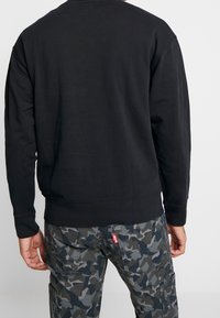 Sudadera negra de manga larga, con puños y dobladillo acanalados, de textura suave. Combinada con pantalones cargo de camuflaje gris que cuentan con bolsillos y costuras.