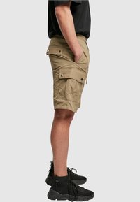 Khaki cargo shorts dengan beberapa kantong samping, pinggang elastis, dan tekstur halus. Dipadukan dengan sepatu sneakers hitam tinggi.