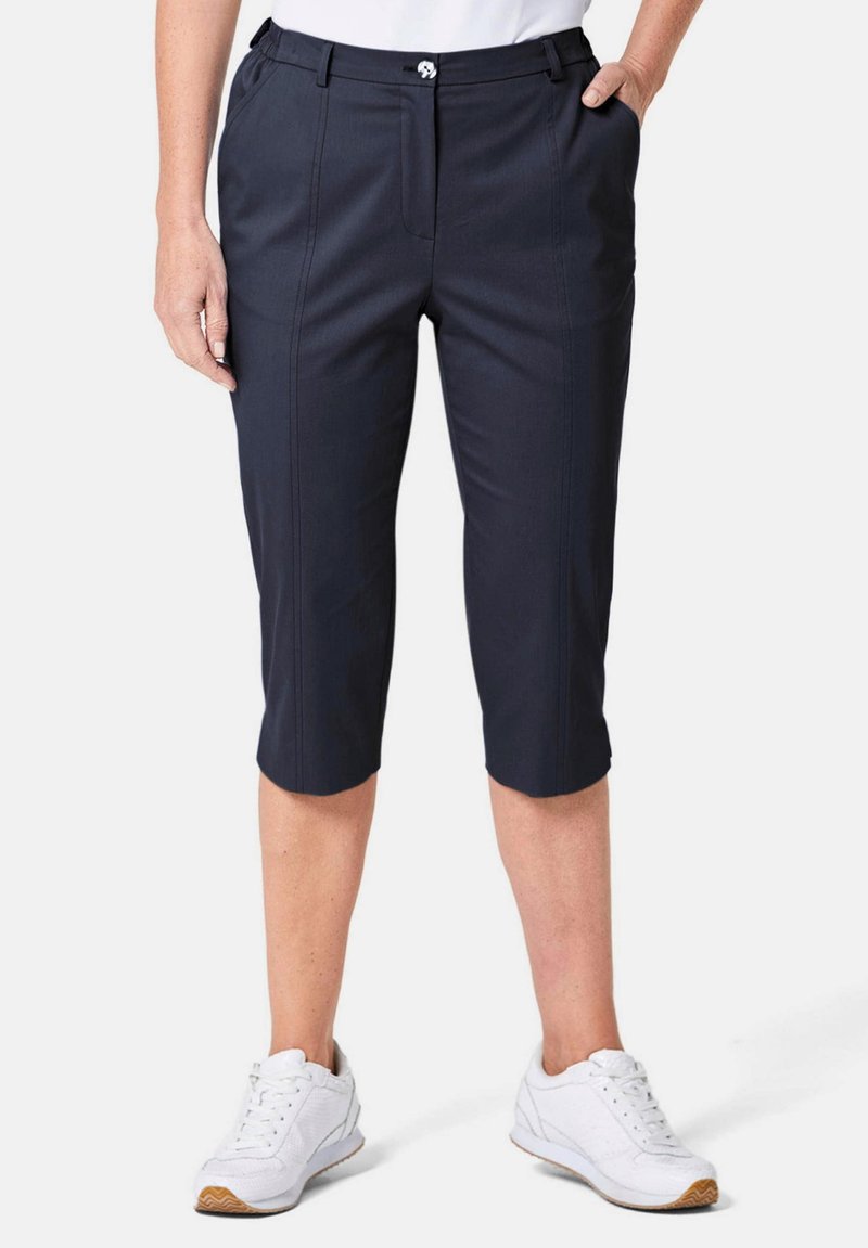 Marineblauwe capri-broek van een gladde stof met een rechte snit, voorzien van voorplooien, een ritsluiting en zijzakken. Gecombineerd met witte sneakers.