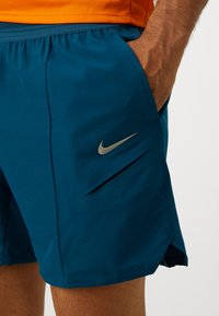Tyrkysové šortky vyrobené z ľahkej tkaniny, s bočnou zipsovou vreckom, elastickým pásom a odrazovým strieborným logom Nike.