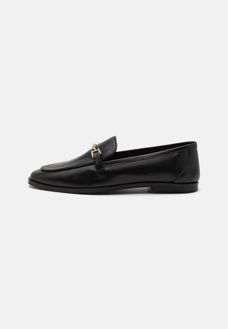 Mocassins en cuir noir avec une semelle plate, un bout arrondi et un accent décoratif en métal doré sur la sangle avant. Texture lisse.