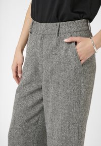Sive herringbone hlače imaju ravni kroj, bočne džepove i opušteni fit. Tkanina ima suptilnu teksturu i krojeni pojas.