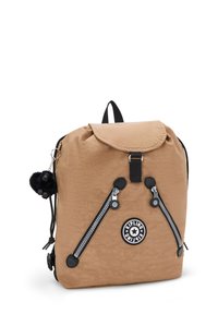 Mochila de tela color arena con cierre de solapa, dos bolsillos con cremallera, acentos negros, un parche con el logo y un llavero con pompón. Textura suave en general.