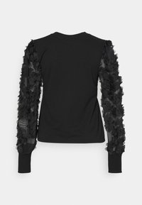 Camiseta negra de manga larga que presenta un cuerpo liso con tela de volante transparente en las mangas, texturizada con apliques florales en capas.