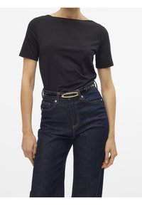 Černá košile s krátkými rukávy a výstřihem do lodi, doplněná o vysoké tmavé džínové kalhoty. Pásek má zlatou oválnou sponu.