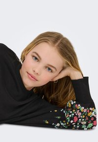 Svart sweatshirt med blommönster på ärmarna i olika färger. Materialet verkar mjukt; har ribbad mudd och avslappnad passform.