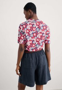 Short-sleeve shirt with a red, white, and blue floral pattern, paired with dark blue shorts featuring two back pockets and a braided belt.