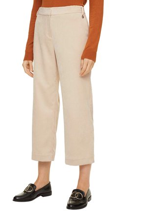 Pantalon beige large et court, associé à des mocassins noirs avec boucle dorée, porté avec un haut à manches longues de couleur rouille.
