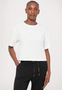 Fehér, rövidujjú, környakú, puha pamutból készült cropped póló, fekete, húzózsinóros részletekkel ellátott nadrággal párosítva.