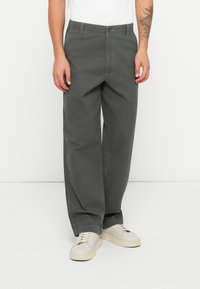 Grey wide-leg trousers made of cotton, featuring visible stitching, a front pocket, and a classic button closure. Worn with white sneakers.