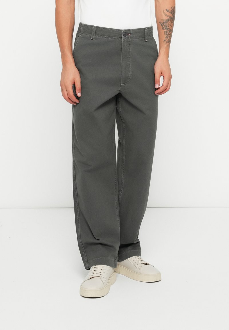 Grey wide-leg trousers made of cotton, featuring visible stitching, a front pocket, and a classic button closure. Worn with white sneakers.