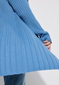 Blauer gerippter Pullover mit langen Ärmeln, verfügt über einen ausgestellten Saum und struktur strick. Der Stoff wirkt weich und leicht.