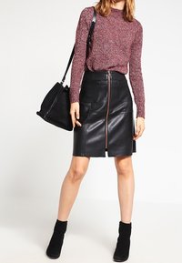 Mekko musta nahkainen kynähame, jossa on edessä vetoketju, yhdistettynä viininpunaisiin neulepuseroihin. Mallilla on päällään mustat nilkkurit ja hän kantaa mustaa käsilaukkua.