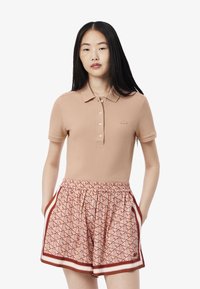 Beige pikétröja med krage och knappar, matchad med mönstrade rosa shorts med geometrisk design och elastisk midja.