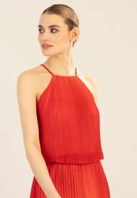 Rotes, plissiertes Kleid mit Häkelkragen, fließendem Stoff und gerafftem Taillieren. Verfügt über zarte Träger und transparente Textur.
