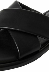 Black leather slide sandal featuring a crossover strap design. Smooth texture with a rounded toe and flat sole. Suitable for casual wear.