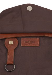 Bruine stoffen tas interieur met leren riem en metalen ring, magnetische drukknoopsluiting en gestikte leren logopatch met de tekst "Gusti Leder Studio."