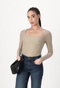 Beige Langarm-Body mit quadratischem Ausschnitt, kombiniert mit dunkelblauen High-Waist-Jeans. Model hält eine schwarze Lederhandtasche.