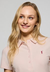 Polo in cotone rosa chiaro con colletto e chiusura a bottoni, caratterizzato da un piccolo logo rosso ricamato sul petto sinistro.