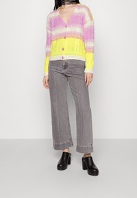 Multicolored knitted cardigan with vertical stripes in pink, yellow, and white; v-neck, button closure, and textured pattern. Paired with grey wide-leg jeans and black heeled clogs.