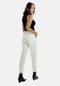 Weiße Joggerhosen mit elastischen Bündchen und Bund, kombiniert mit einem schwarzen ärmellosen Oberteil. Schwarze Knöchelstiefel mit strukturiertem Finish.