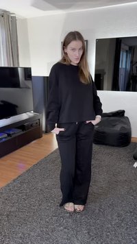 Black sweatshirt with a relaxed fit, round neckline, and long sleeves. Paired with black pants featuring pockets, worn with sandals.
