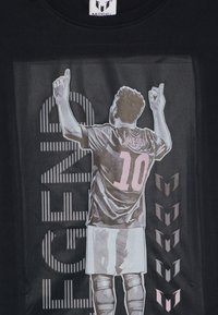 Svart T-skjorte med et grafisk bilde av en stående figur med hevede armer, iført en drakt med "MESSI" og "10". Merkbare detaljer i rosa.