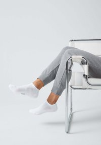 Weiße Knöchelsocken aus Baumwollmischung mit einer strukturierten Fußsohle, kombiniert mit grauen Jogginghosen, die auf einem chromfarbenen Stuhl liegen.