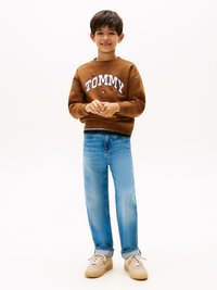 Smešani dukserica smeđe boje sa "TOMMY" logom, plave ravne farmerke i bež patike. Glatka tkanina i opušten kroj kroz celu figuru.