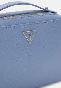 Blauwe handtas met een textuur oppervlak, gouden details en een driehoekig logo. Voorzien van een bovenhandvat en ritssluiting.