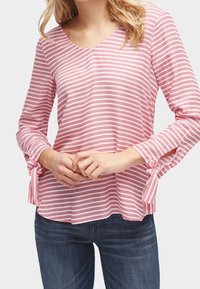 Maglietta a maniche lunghe a righe rosa e bianche con scollo a V. Presenta un tessuto testurizzato e lacci ai polsini delle maniche. Abbinata a jeans scuri.