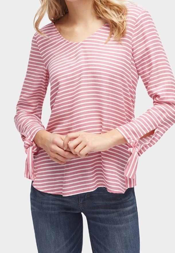 Maglietta a maniche lunghe a righe rosa e bianche con scollo a V. Presenta un tessuto testurizzato e lacci ai polsini delle maniche. Abbinata a jeans scuri.