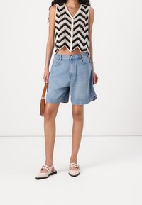 Háčkovaný krátký top v černobílém vzoru s chevronem; světle modré džínové šortky; béžové boty na blokovém podpatku s páskem kolem kotníku; hnědá kabelka.