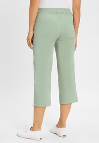Lichtgroene cropped broek met een elastische tailleband, twee achterzakken en een gladde textuur. Gecombineerd met witte sneakers.