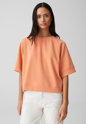 Short-sleeve, coral sweatshirt in a soft, lightweight fabric with a relaxed fit and ribbed neckline. Paired with white pants.