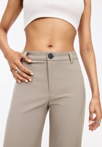 Beige tailored trousers with a smooth texture, featuring a button closure, belt loops, and front pockets. Styled with a fitted crop top.