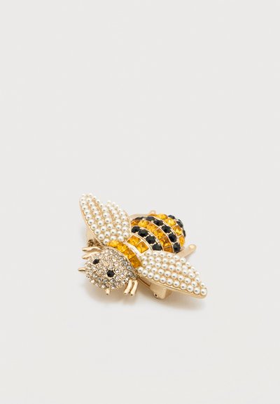 Καρφίτσα σε σχήμα μέλισσας με μεταλλικό χρυσό τόνο, διακοσμημένη με διαφανείς, κίτρινες και μαύρες στρας, με υφή που θυμίζει μαργαριτάρι στις φτερούγες.