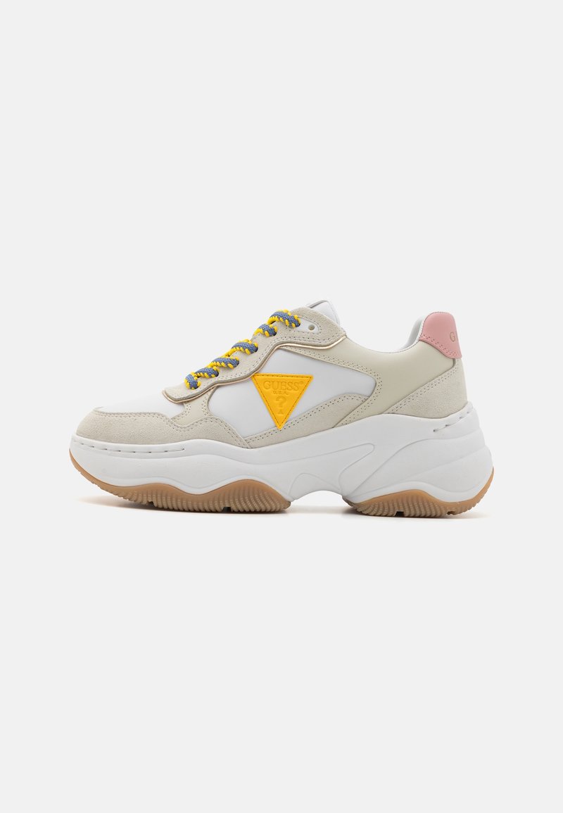 Baskets épaisses blanches et beiges avec lacets jaunes et bleus, patch logo triangulaire jaune, languette rose au talon et semelle épaisse texturée.