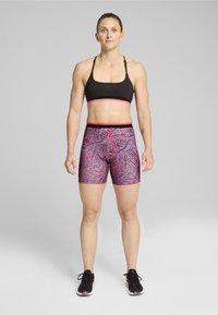Sujetador deportivo negro con acentos rosas, combinado con shorts de estampado abstracto en rosa. El tejido parece elástico y tiene una textura suave.