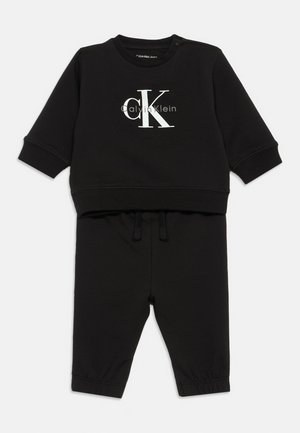 Conjunto de sweatshirt e calças para crianças negras, feito de tecido macio. Apresenta um logo branco "CK", punhos canelados e uma cintura elástica com cordões.
