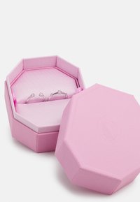 Achtseitige pinke Schmuckschatulle mit strukturierter Oberfläche. Enthält drei Ringe mit klaren Steinen, die vor einem sanften pinken Innenraum angeordnet sind.