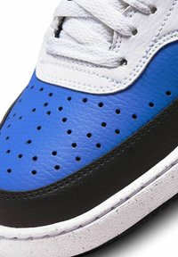 Sneaker blu in pelle con tomaia perforata, lacci bianchi, suola nera e accenti texturizzati. Presenta una finitura liscia e cuciture a contrasto.