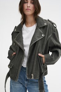 Veste de moto en cuir gris avec accessoires en métal argenté, fermeture éclair asymétrique et coupe oversize. Associée à un t-shirt blanc et un jean bleu.