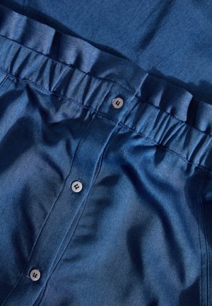 Donkerblauwe denim blouse met een gerimpelde tailleband, voorzien van vijf knopen en een soepele textuur. Zichtbaar stikseldetail.