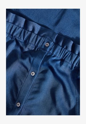 Donkerblauwe denim blouse met een gerimpelde tailleband, voorzien van vijf knopen en een soepele textuur. Zichtbaar stikseldetail.