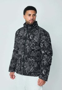 Doudoune noire à fleurs avec un col haut, tissu texturé et fermeture éclair ; présente un motif de fleurs blanches et grises.