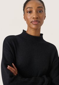Pulover negru cu guler înalt, realizat dintr-o țesătură moale, având mâneci lungi și o croială lejeră, cu o textură subtilă și fără modele vizibile.