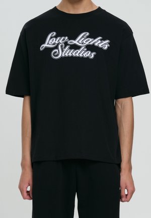 T-shirt en coton noir avec texte brodé en blanc « Low Lights Studios » en police incurvée et audacieuse. Manches courtes et coupe ample.