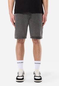 Gray denim shorts with a straight cut, knee-length, featuring a frayed hem. Worn with black and white sneakers and white socks.